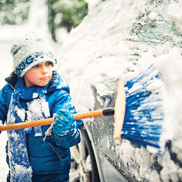 A child brushing off a vehicle covered in snow