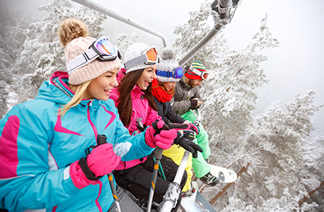 Four AAA Members riding a ski lift with snowy trees in the background.
