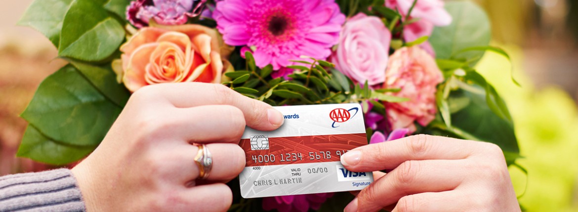 A hand passing an AAA Visa Credit Card over to another hand, flower bouquet in background