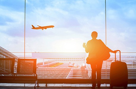 an airplane flying off into the sunset while a AAA member looks on with luggage