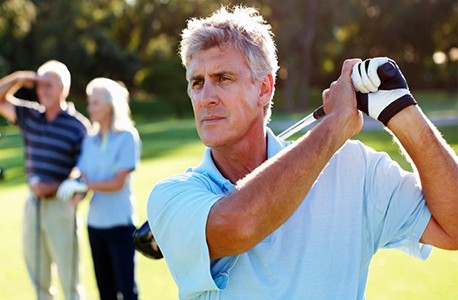 AAA member finishing his swing on a golf course while two other AAA members look on.