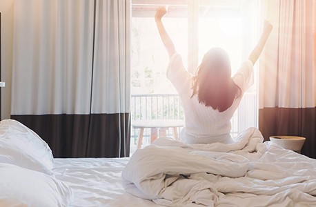 Female AAA member waking up in a hotel in the morning and stretching in front of the window