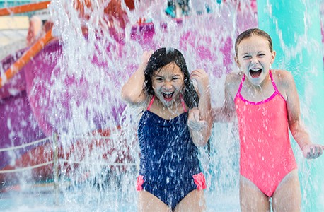 Two young girls playing in a waterpark, standing under falling water